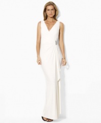 This Lauren by Ralph Lauren elegant floor-grazing gown is rendered in a sleeveless silhouette with a crossover V-neckline secured with an encrusted brooch and finished with a graceful ruffle the length of the skirt.